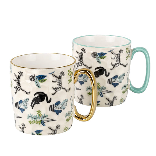 Two ceramic mugs with a white base, decorated with black and blue wild animals and botanical patterns, with one featuring a gold handle and the other a mint green handle.